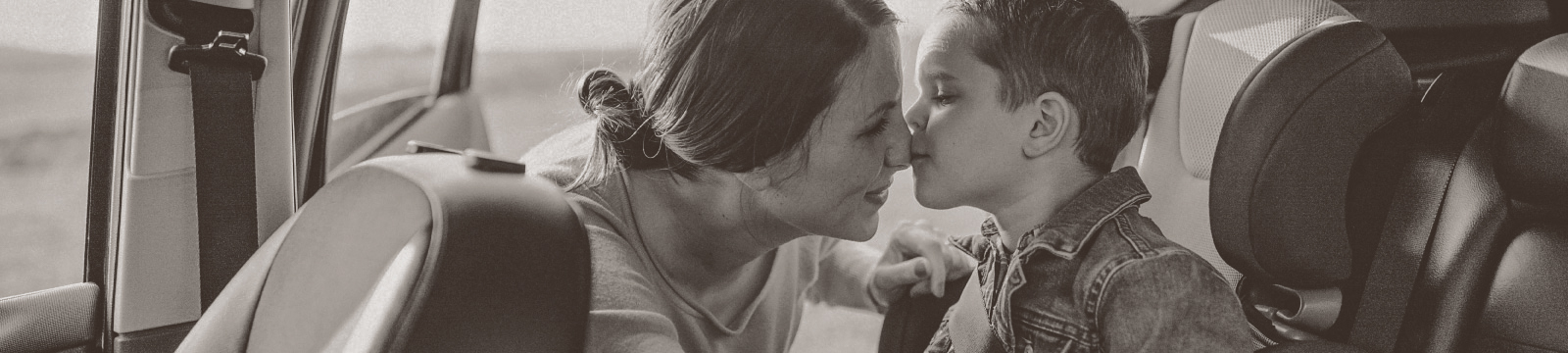 Young boy in car seat kisses his mother on the nose.