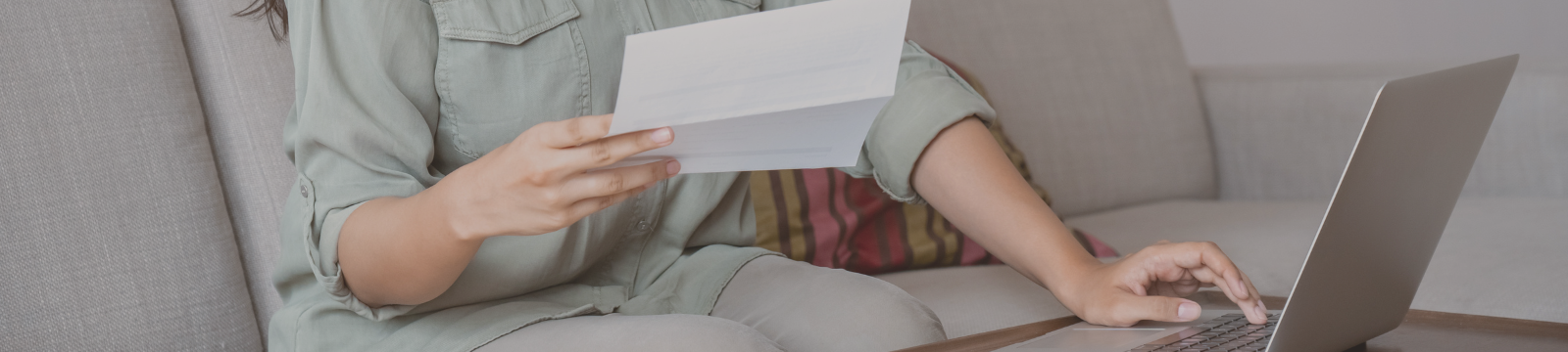 Person holding a bill and has one hand on the computer